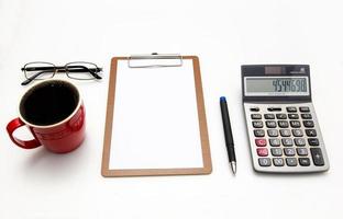 ovanifrån av skrivbordet på vit bakgrund blankt papper, penna, miniräknare, glasögon, kaffe. ekonomisk planering och arbetskoncept. foto