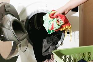 närbild av en kvinnas hand som lägger smutsiga kläder i tvättmaskinen foto