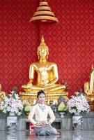 thailändsk kvinna som sitter framför buddhastatyn foto