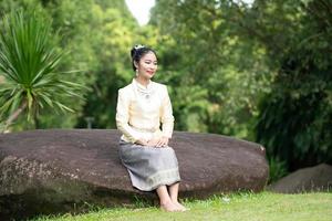 elegant thailändsk kvinna i thailändsk klänning prydd med värdefulla smycken promenader med blomstergirlanger i thailändska tempel foto