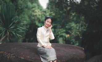 elegant thailändsk kvinna i thailändsk klänning prydd med värdefulla smycken promenader med blomstergirlanger i thailändska tempel foto