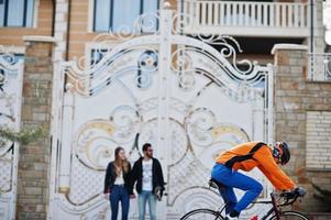 cykelryttare rör sig mot coola par som står med longboard mot höga grindar. foto