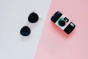 kreativ platt lekmannastil i modekoncept med kamera och solglasögon på minimal färgbakgrund, ovanifrån foto