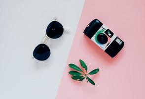 kreativ platt lekmannastil i modekoncept med kamera och solglasögon på minimal färgbakgrund, ovanifrån foto