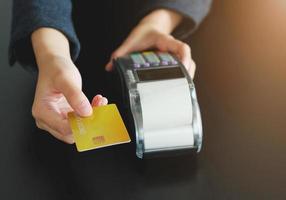 en kvinna som använder hand kreditkortssvepmaskin för att sälja produkter i butiken. begreppet utgifter via kreditkort. foto