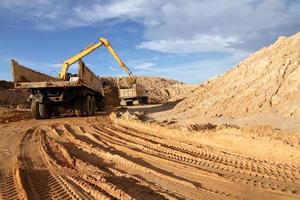 tung grävmaskin lastning dumper lastbil med sand i stenbrott över blå himmel foto