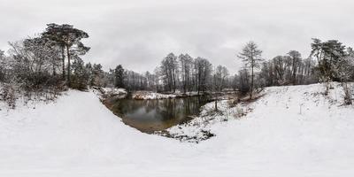 vinter full sfärisk hdri panorama 360 graders vinkelvy nära smal snabb flod i snöig tallskog med grå blek himmel i ekvirektangulär projektion. vr ar innehåll foto