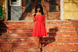 snygg trendig afro frankrike lockig kvinna poserade på höstdagen i röd klänning. svart afrikansk kvinnlig modell. foto