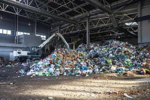 grävmaskin staplar skräp i stor hög vid sortering av modern avfallsåtervinningsanläggning. separera och sortera sophämtning. återvinning och lagring av avfall foto