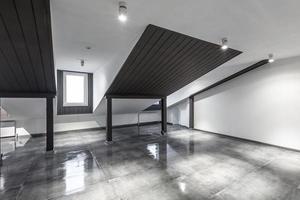 Tomt omöblerat loft mansardrumsinredning med träpelare och vått betonggolv på taknivå i svart och hel stilfärg foto