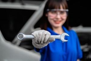 närbild av tekniker eller bilreparation. kvinna reparatör håller metall skiftnyckel i garage. bilreparationsservicekoncept. bil prototyp koncept. underhållstekniker foto