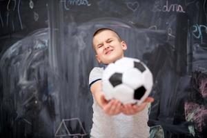 glad pojke som håller en fotboll framför svarta tavlan foto