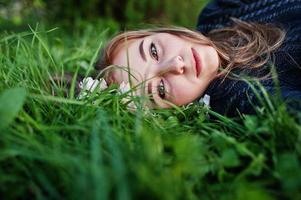ung brunett flicka liggande på grönt gräs med grenar av blomma träd. foto