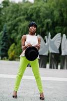 fantastisk afrikansk amerikansk modellkvinna i gröna byxor och svart hatt poserade i parken. foto