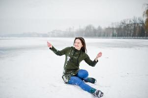 rolig flicka slitage på lång grön tröja och jeans, vid frusen sjö i vinterdag. foto