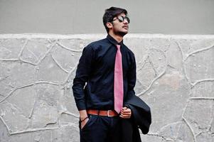 ung indisk man på svart skjorta, slips och solglasögon poserade utomhus. foto