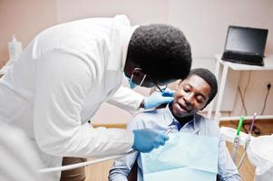 afrikansk amerikansk man patient i tandläkarstol. tandläkare kontor och läkare praktik koncept. professionell tandläkare som hjälper sin patient vid tandläkare. borra patientens tänder på kliniken. foto