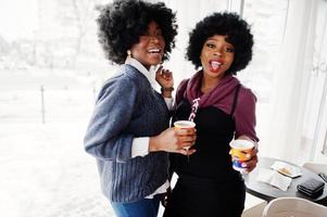 två lockigt hår afrikansk amerikansk kvinna bär tröjor med koppar te poserade på café inomhus. foto