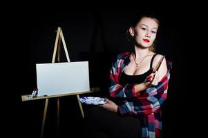 vacker kvinna konstnär målare med penslar och oljeduk poserar i studio isolerad på svart. foto