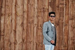 casual ung indisk man i silver kavaj och solglasögon poserade mot trä bakgrund. foto