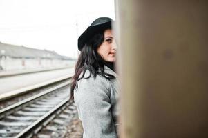 brunett flicka i grå rock med hatt i järnvägsstationen. foto