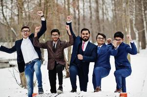grupp av fem indisk affärsman i kostym poserade utomhus i vinterdag i Europa, händerna upp och visa glada känslor. foto