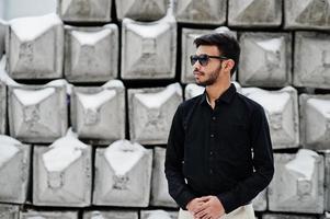 casual ung indisk man i svart skjorta och solglasögon poserade mot stenblock. foto