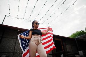 snygg afrikansk amerikansk kvinna i solglasögon poserade utomhus med USAs flagga. foto