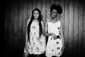 två svarta afrikanska flickvänner på sommarklänningar poserade mot mörk trä bakgrund. foto