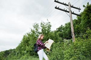 porträtt av en vacker blond tjej i tartanskjorta som går med en karta på landsbygden. foto