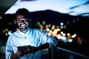 ung afro man på gatan på natten med hjälp av surfplatta foto