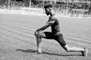 afrikansk amerikansk manlig idrottare i sportkläder gör stretching övning på stadion. foto