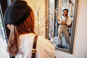 afrikansk amerikansk kvinna i overall och basker mot spegel i mjukt ljus rum. foto