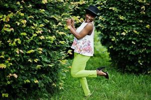 fantastisk afrikansk amerikansk modellkvinna i gröna byxor och svart hatt poserade i parken. foto