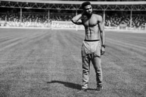 stilig sexig afrikansk amerikansk muskulös bar överkropp man på jeansoveraller poserade på grönt gräs på stadion fotbollsplan. fashionabla svart man porträtt. foto