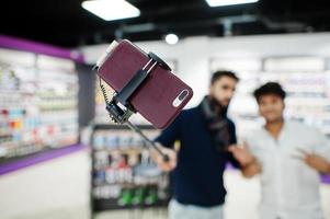 närbild foto av mobiltelefon på monopod stick mot två indianer mans kund köpare aking selfie. sydasiatiska folk och teknik koncept. mobiltelefon butik.