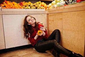 flicka i rött håller två paprika på frukt butik. foto