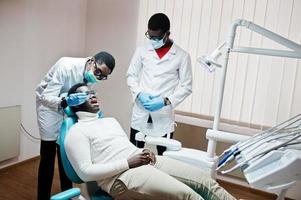 afrikansk amerikansk man patient i tandläkarstol. tandläkare kontor och läkare praktik koncept. professionell tandläkare som hjälper sin patient vid tandläkare. foto