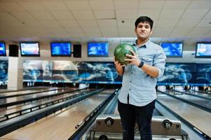 snygg asiatisk man i jeansskjorta stående vid bowlinghall med boll till hands. foto