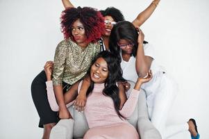 glada ljusa positiva stunder av fyra afrikanska flickor. ha kul och ler på stol mot vit tom vägg. härliga stunder av fyra kramas bästa vänner. foto
