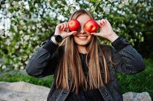 ung brunett flicka på jeans sitter på pläd mot våren blossom träd och visa äpple ögon. foto