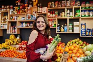 flicka i rött håller olika grönsaker på frukt butik. foto