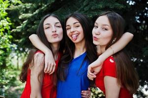 tre tonåringar flicka i blå och röda klänningar poserade utomhus och visar tonque. foto