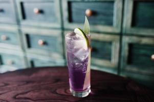 alkoholhaltig lång violett cocktail med is i glas vid barbordet. foto