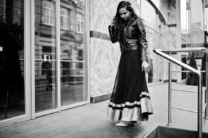 söt indisk flicka i svart saree klänning och skinnjacka poserade utomhus på gatan. foto