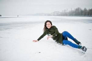 rolig flicka slitage på lång grön tröja och jeans, vid frusen sjö i vinterdag. foto