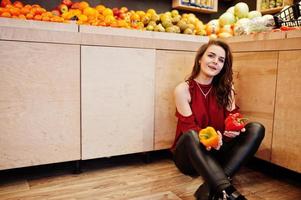 flicka i rött håller två paprika på frukt butik. foto