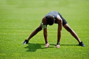 afrikansk amerikansk manlig idrottare i sportkläder gör stretching övning på stadion. foto