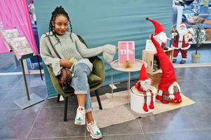 afrikansk kvinna poserade i tröja och jeans poserade på köpcentret mot juldekoration och nyårstema. foto