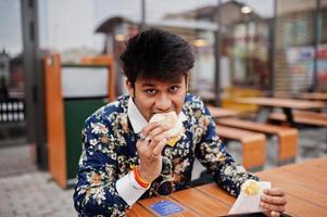 attraktiv och stilig snygg indisk man bär på skjorta äta hamburgare och pommes frites på terrassen på moderna loungecafé på sin arbetsrast. foto
